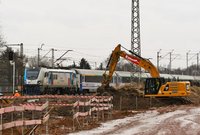 Koparka przy pracach ziemnych. Obok po torze przejeżdżający pociąg, fot. Martyn Janduła