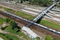 Widok z góry na konstrukcję kładki nad torami linii średnicowej i przejeżdżający pociąg, fot. Artur Lewandowski