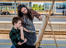 Ujęcie na prowadzącą rozmawiającą z uczestniczką i malującą obraz, 11.06.2022 r., Źródło PKP PLK S.A. (1)